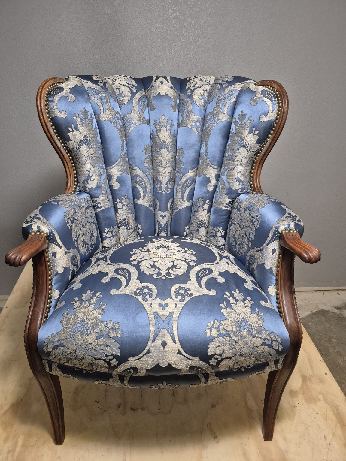 Finished blue patterned channel-back chair with exposed wooden arms and decorative nail trim