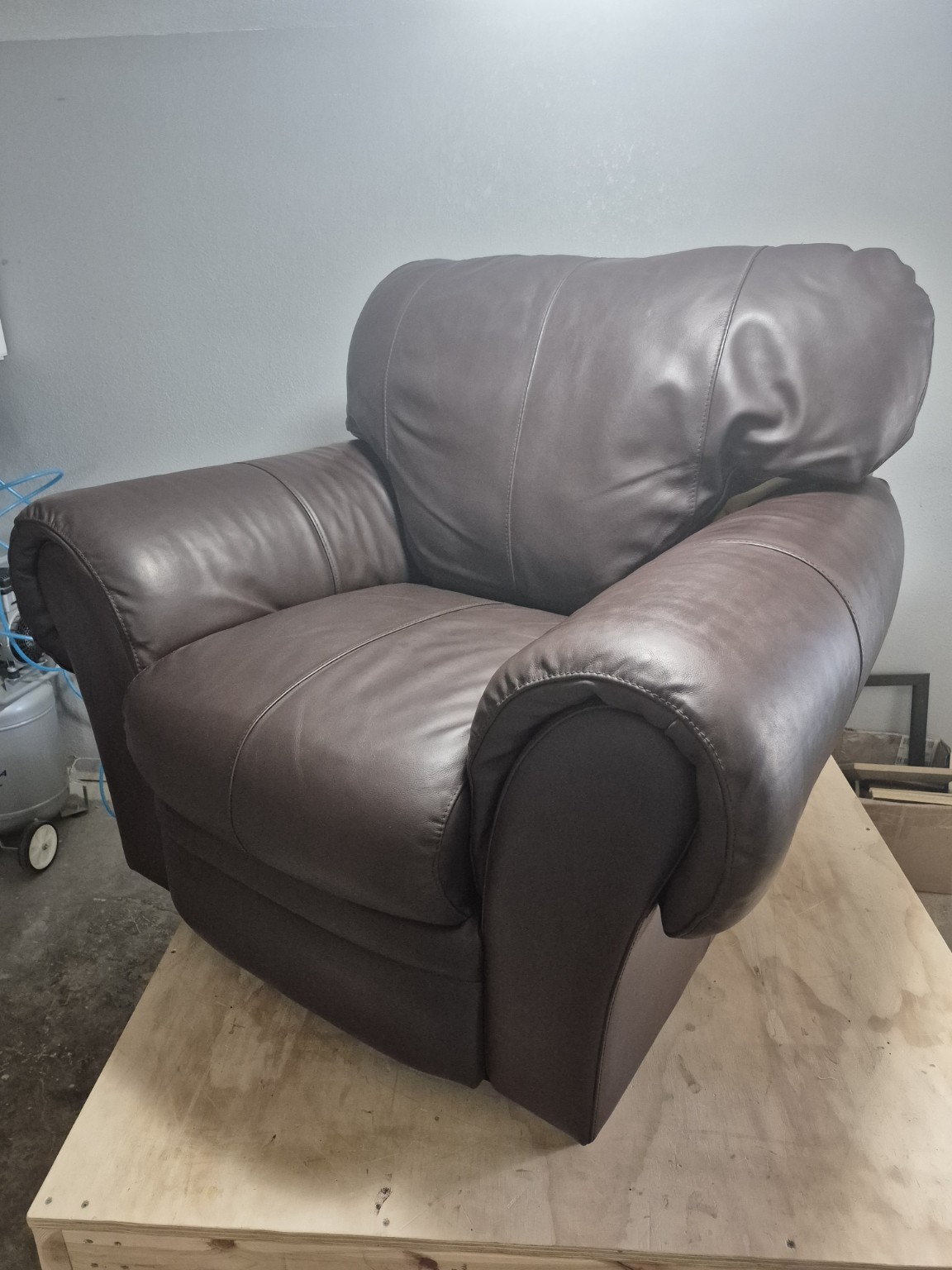 Finished brown upholstered armchair with padded arms and back, photographed on the workbench